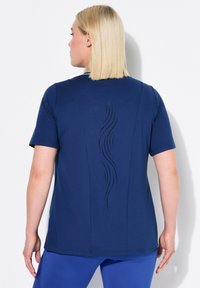 Camisa de manga corta de color azul marino con un diseño perforado curvado en la parte posterior, hecha de una tela suave y elástica, y con cuello redondo.