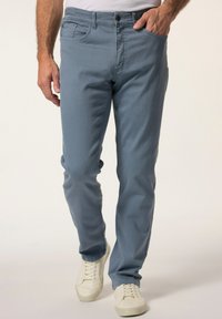 Jeans ajustados de color azul claro con diseño de cinco bolsillos, fabricados en una mezcla de algodón, con una textura sutil y un solo botón de cierre en el frente, combinados con zapatillas blancas.