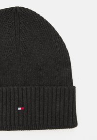 Schwarze Strickmütze mit geripptem Muster, die am Saum ein kleines gesticktes Logo in Rot, Weiß und Blau aufweist.