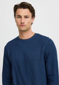 Maglione a maniche lunghe blu navy con un motivo a maglia testurizzata, scollatura tonda e un delicato dettaglio del logo sul petto.