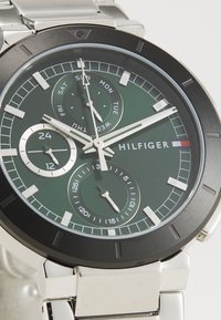 Montre en acier inoxydable argenté avec un cadran vert, une lunette noire et trois sous-cadrans. Présente des index horaires blancs et un indicateur de date.