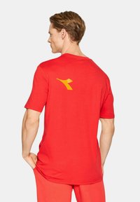 Maglietta rossa a maniche corte in morbido tessuto, con un logo giallo sul retro. Il design presenta un classico collo a giro e una vestibilità rilassata.