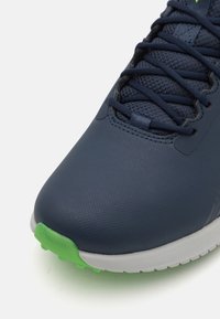 Pantofii sport navy cu un brâu texturat, prezintă o talpă verde și o intermediară albă. Include șireturi și secțiuni din plasă respirabilă.