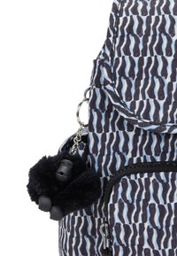 Zaino blu e nero con un motivo a disegni, caratterizzato da un esterno testurizzato, con un ciondolo di un gorilla nero peloso attaccato alla zip.