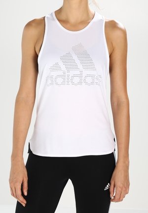 Vrouw draagt een wit mouwloos sporttopje met geperforeerd Adidas-logo en zwarte Adidas legging.