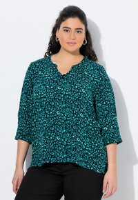 Blusa turchese con motivo leopardato, maniche a 3/4, scollatura a V e pieghe sottili sul davanti. Realizzata in tessuto leggero e strutturato.