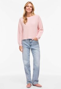Pull en maille rose clair avec un motif texturé, associé à un jean denim bleu taille haute. Chaussures confortables à enfiler, coupe décontractée.