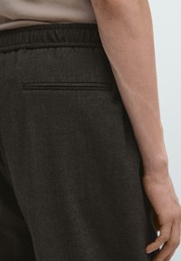 Pantaloni grigio scuro strutturati con vita elastica e tasca posteriore. Il tessuto presenta un sottile motivo intrecciato e una finitura morbida.