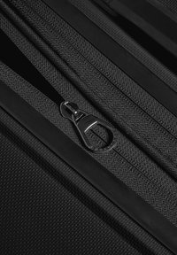 Primo piano di una zip nera con tessuto strutturato e tiretto in metallo su una superficie nera strutturata.