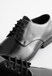 Black leather shoes featuring a smooth finish and perforated detailing on the sides, with black laces and a low heel.
