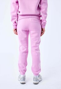 Roze, zachte joggingbroeken met elastische boorden en een achterzak. Gecombineerd met witte sneakers met zilveren accenten.