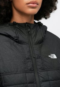 Czarna kurtka puchowa z wzorem pikowanym, z kapturem, z przodu na zamek błyskawiczny i ściągaczem. Logo na lewej części klatki piersiowej.