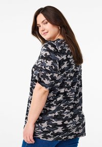 T-shirt à manches courtes avec un motif camouflage noir, gris et gris clair. Coupe décontractée avec un col rond et une texture douce.