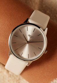 Silberne Armbanduhr mit gebürstetem Zifferblatt, minimalistischen Stundenmarkierungen und einem weißen Lederarmband. Enthält den Markennamen "regal" und ein Uhrwerk aus Japan.