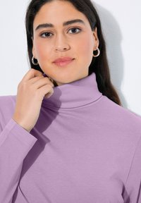 Levandulový rolák z měkké látky. Má dlouhé rukávy a přiléhavý střih s hladkou texturou. Jednoduché šití.