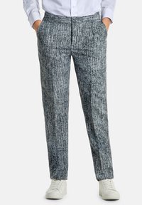 Pantaloni leggeri e con motivo in grigio e nero con una finitura testurizzata. Presentano tasche anteriori e una chiusura con bottone, indossati con sneaker bianche.
