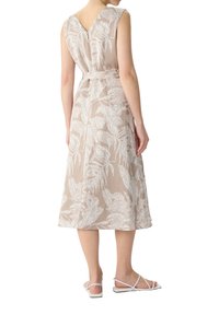 Beżowa sukienka bez rękawów z białym wzorem liści, z tylnym dekoltem w kształcie litery V, z dopasowaną talią i zwiewną spódnicą o długości midi. Połączona z sandałami na cienkich paskach.