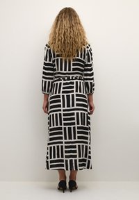 Robe à motifs noir et blanc avec des manches longues, une taille cintrée et une jupe fluide. Le tissu a une texture lisse et des motifs géométriques.