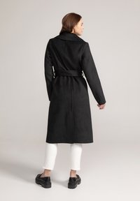 Zwarte wolmix jas met een ceintuur in de taille, gekartelde kraag en lange mouwen. Glad textuur en middenlange ontwerp, geschikt voor verschillende gelegenheden.