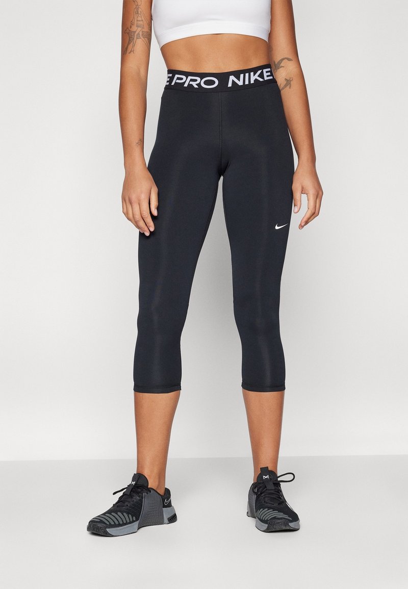 Leggings capri negros con una cinturilla ancha que presenta "PRO NIKE" en blanco. Textura suave con un pequeño logo de Nike en blanco en el muslo.