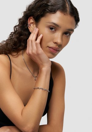 Silberschmuck zeigt ein zartes Kettenarmband mit abwechselnden Gliederdesigns. Das Model trägt eine schlichte Silberkette und posiert nachdenklich.