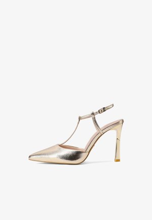 Escarpin doré à bout pointu avec bride en T et boucle à la cheville sur fond blanc.