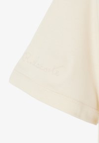 T-shirt en coton couleur crème, manches courtes, avec le texte brodé "R. lacoste" près de l'ourlet, texture lisse, couture nette.