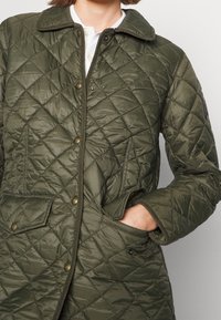 Mönstrad grön jacka med krage, tryckknappar, diagonala sömmar, två framsidiga fickor och en strukturerad yta.