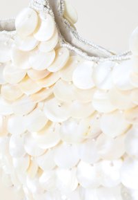 Beaded handbag covered in white, round shell discs. Features a fabric lining and a braided beaded trim along the edge.