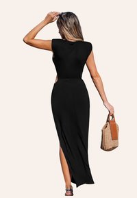 Robe maxi noire avec des manches courtes et des découpes latérales. Dispose d'une fente haute et d'une texture lisse. Modèle tenant un sac tissé avec des accents en cuir.