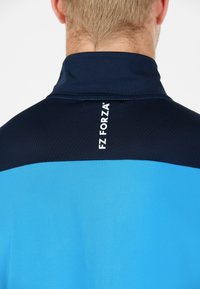 Kortärmad sporttröja med marinblå krage och överdel, som övergår till en ljusblå kropp, med "FZ FORZA"-logotypen iögonfallande synlig.