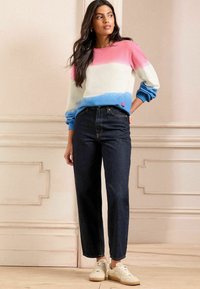 Maglione a blocchi di colore con sezioni rosa, bianche e blu, abbinato a jeans scuri a vita alta e sneakers bianche. Tessuto morbido, vestibilità rilassata.
