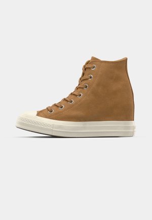 Vysoké tenisky vyrobené z hnedej semišovej kože s bielou gumovou podrážkou a špičkou, s kovovými očkami a plochým šnurovaním.