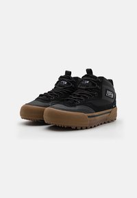 Sorte mid-top joggesko laget av semsket skinn og syntetisk materiale, med en gummisåle med teksturert grep, snøring og et merket åkle.