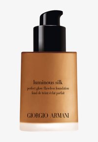 Botella de vidrio marrón con un dispensador negro; etiquetada como "luminous silk perfect glow flawless foundation" en fuente negra en el costado.