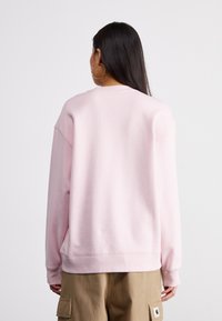Felpa rosa chiaro con una texture morbida, maniche lunghe e polsini a costine. Presenta una vestibilità comoda, abbinata a pantaloni cargo color khaki.