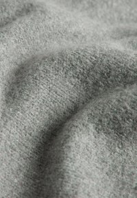 Miękka, teksturowana szara tkanina z dzianym wzorem, ukazująca delikatne fale i fałdy, podkreślająca jej przytulne i dotykowe właściwości.