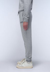 Grijze katoenen sweatpants met een elastische tailleband en boorden, voorzien van een klein logo aan de bovenkant van het bovenbeen, gecombineerd met witte sneakers.