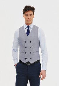 Szary, wzorzysty, podwójnie zapinany kamizelka z sześcioma czarnymi guzikami, w zestawieniu z jasnoniebieską koszulą i ciemnoniebieskim paskiem oraz spodniami.