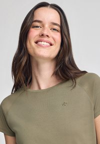 Camicia corta a maniche corte verde oliva con scollatura rotonda e ricamo del logo discreto sul petto sinistro. Tessuto morbido e liscio con una vestibilità rilassata.