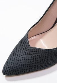 Escarpin noir à bout pointu avec une surface texturée ressemblant à un fin maillage, dotée d'un design à découpes basses et d'un intérieur lisse de couleur claire.