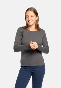 Maglietta grigia a maniche lunghe realizzata in tessuto morbido, con scollatura rotonda e design aderente, abbinata a jeans blu.