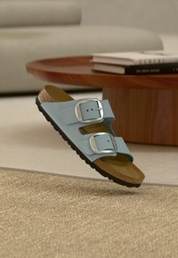 Ανοιχτό μπλε σανδάλια με δύο ρυθμιζόμενα λουράκια με μεταλλικές αγκράφες, πάτο από φελλό και υφή μαύρης καουτσούκ σόλας.