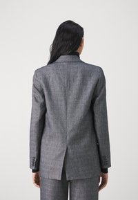 Blazer gris sur mesure avec un motif texturé subtil, col à revers cranté et fentes doubles à l'arrière. Comprend des poignets boutonnés et un design élégant.