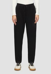 Zwarte sweatpants van zachte stof, met een elastische tailleband met trekkoord, een tapse pasvorm en zijzakken. Gekocht met witte sneakers.