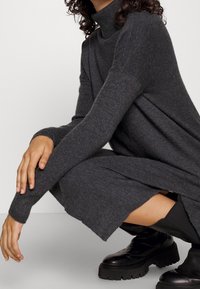 Wielokolorowa sukienka z dzianiny w kolorze węgla, z długimi rękawami, o luźnym kroju i bocznych rozporkach. Noszona z czarnymi botkami do kolan.