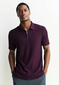 Krátky rukáv, tmavo fialová rebrovaná polo košeľa s polovičným zipsom vpredu a klasickým golierom. Vyznačuje sa textúrovanou tkaninou a voľným strihom.