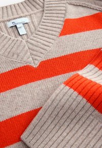 Beige sweater med orange og beige vandrette striber. V-halsdesign, ribbet tekstur, med et mærke mærket "Premium Collection."