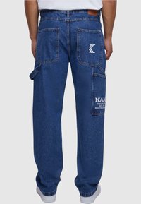 Pantalones cargo de denim, azul oscuro, con múltiples bolsillos, parche de marca, costuras en contraste y un corte relajado. Tejido texturizado con un acabado duradero.