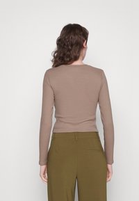 Maglia marrone a maniche lunghe realizzata in tessuto morbido, con scollatura arrotondata e silhouette aderente, abbinata a pantaloni verdi a vita alta.
